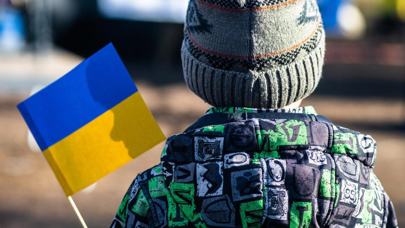 Back of refugee child waving a Ukrainian flag